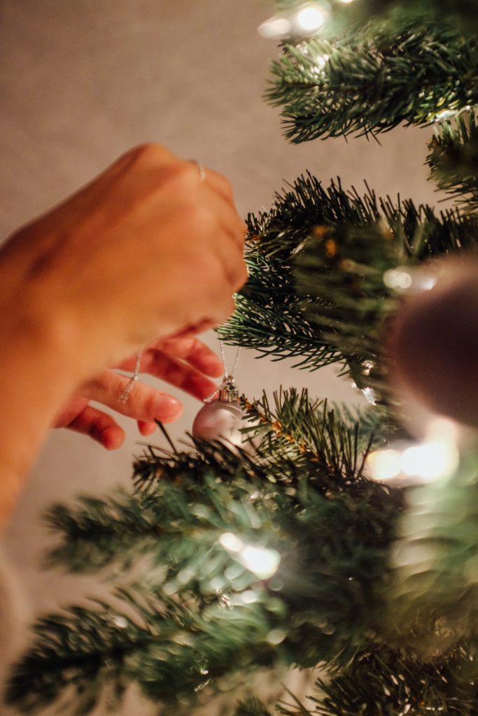 Matrimonio a tema natalizio: mano che decora l'albero di Natale con una pallina